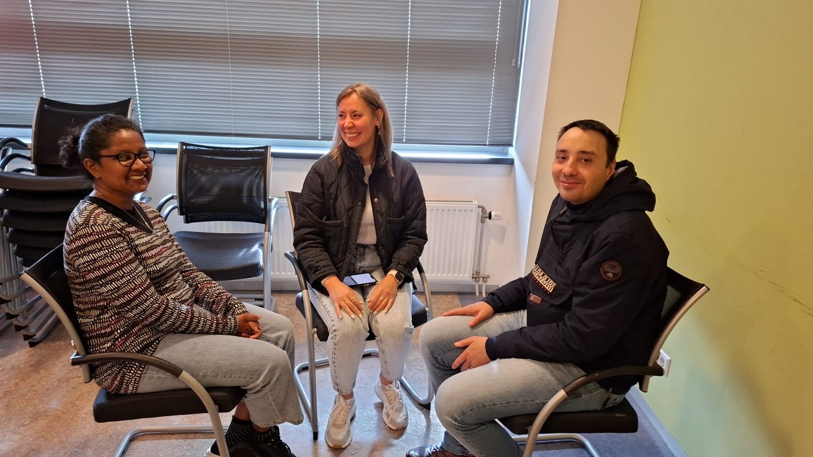 Drie cursisten oefenen lachend een gesprek in een kring