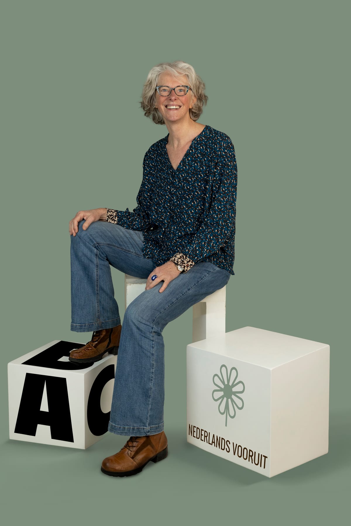 Saskia Niessink zit lachend op witte letterblokken, een ervan met het logo van Nederlands Vooruit