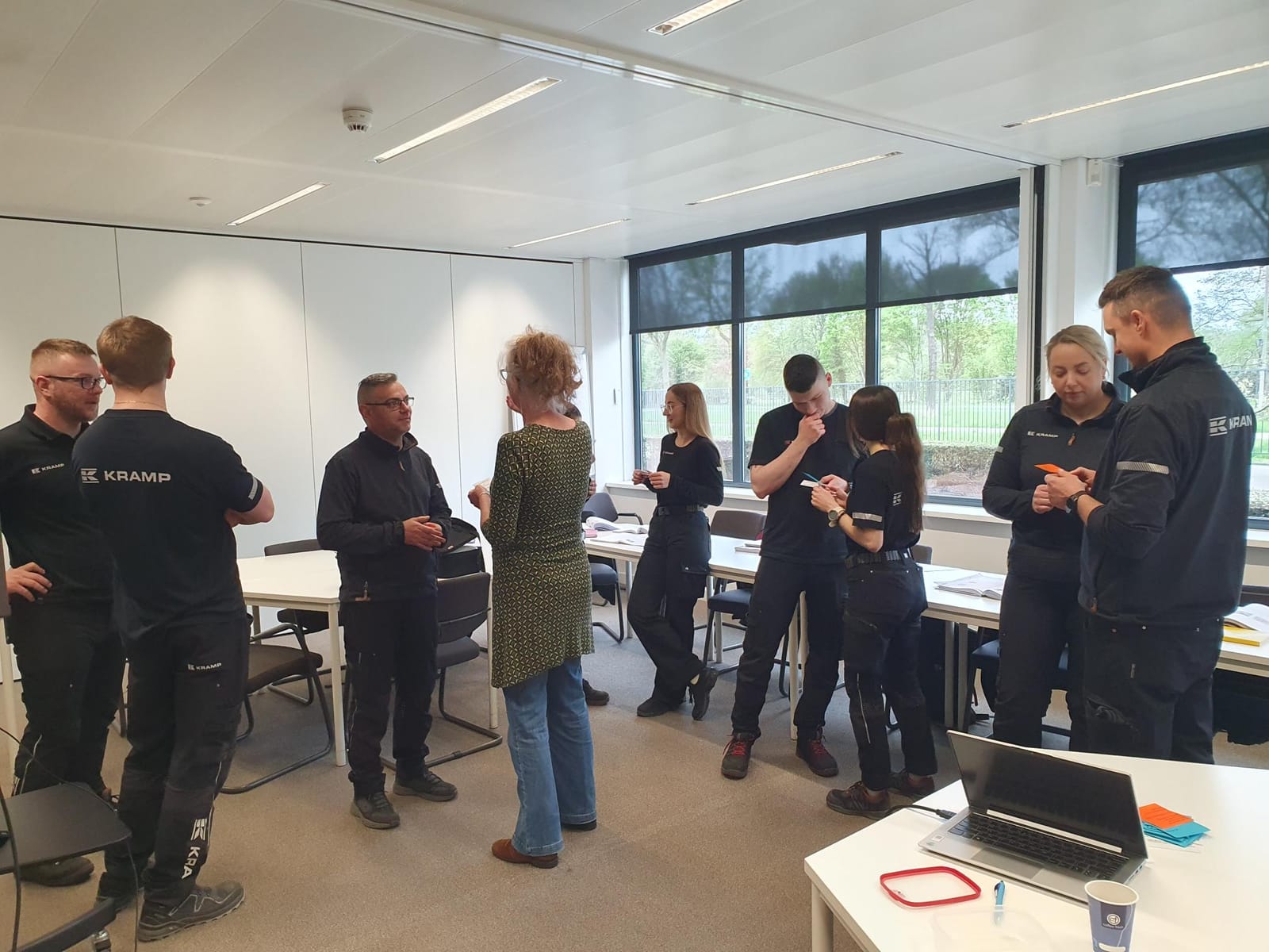 Saskia Niessink in gesprek met een medewerker, terwijl collega's in tweetallen oefenen