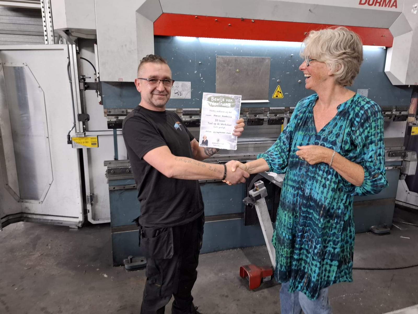 Saskia Niessink reikt in een productiehal een bewijs van deelname uit aan een medewerker
